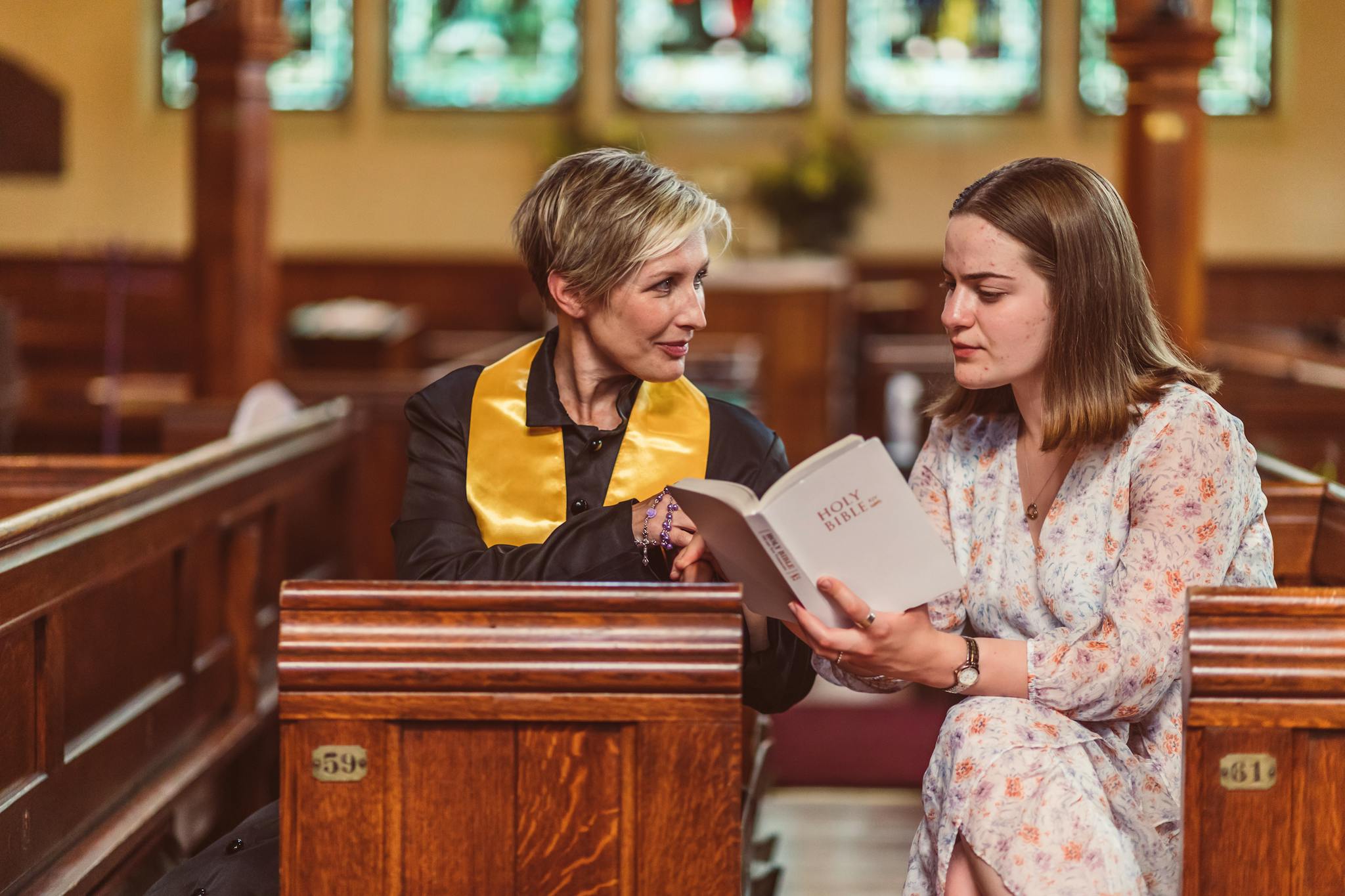 Two women sit in church pews, reading the Holy Bible together.